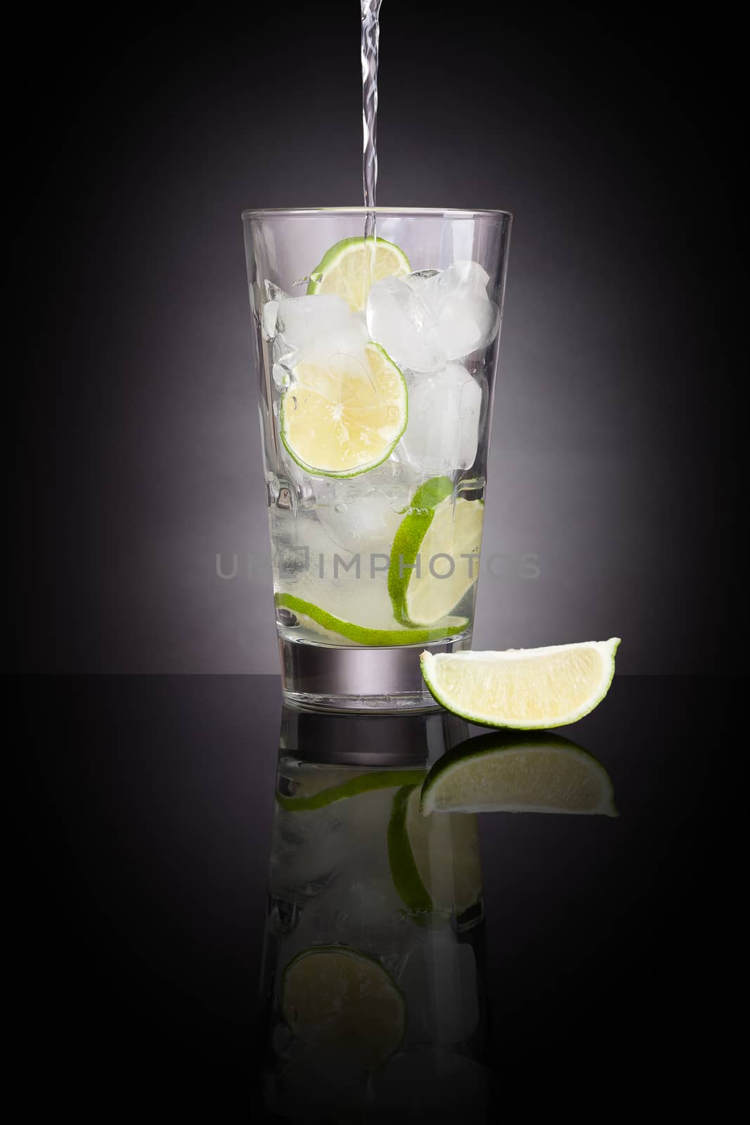Pouring water into a glass full with ice cubes and lime slices. Healthy water drinking. Drinking regime. 