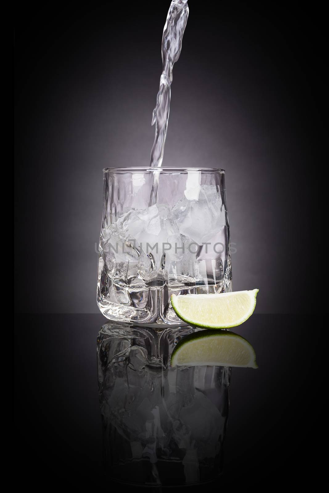 Drinking vodka. Pouring vodka into luxurious shot glass with lime on black background with reflection. Traditional transparent alcohol drinking.