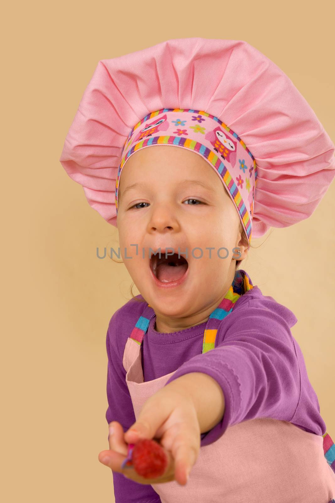 Little cute girl with chef hat eating raspberry. Culinary concept.