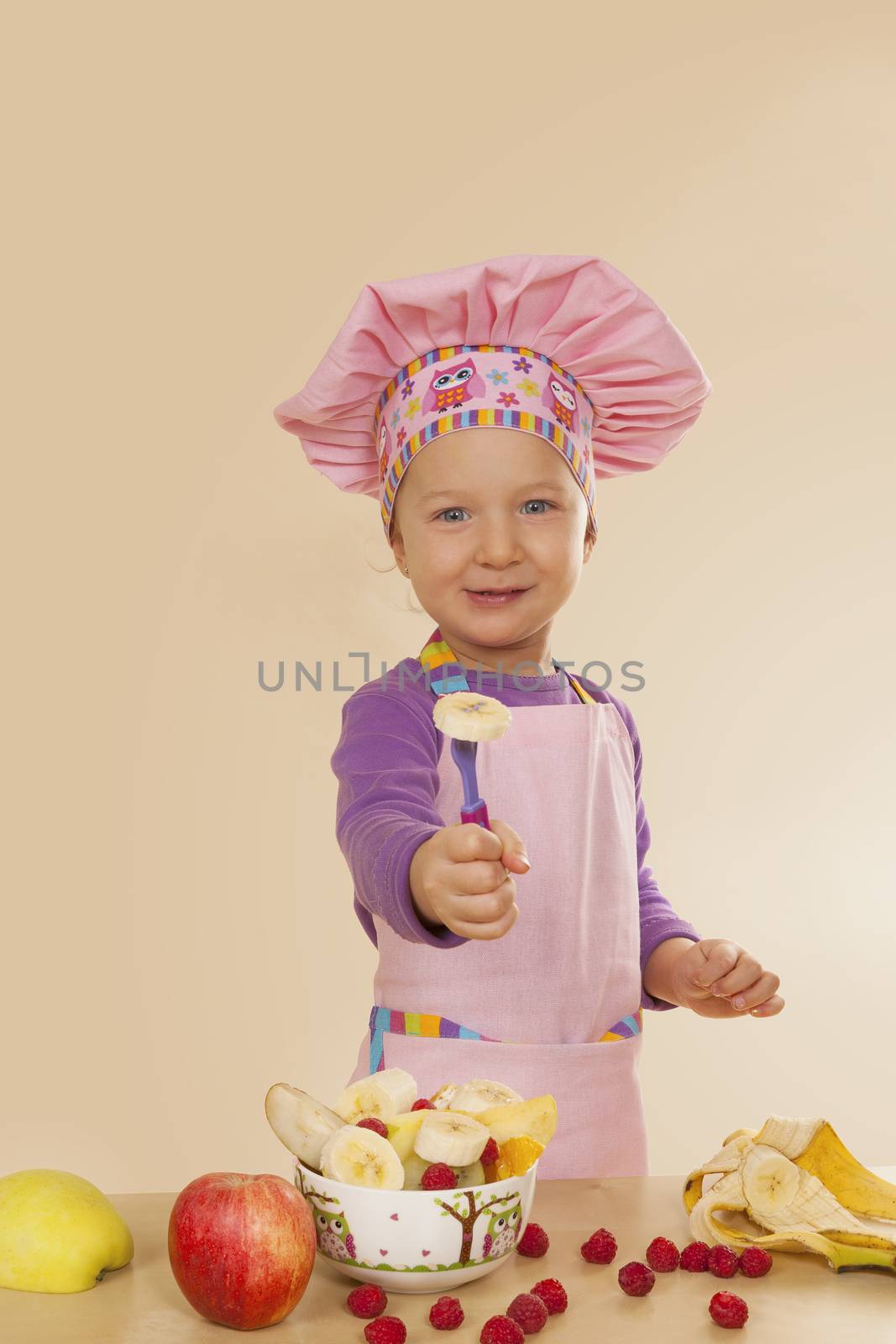 Little girl in purple cook hat and tablier making fruit salad. Healthy eating habits. 