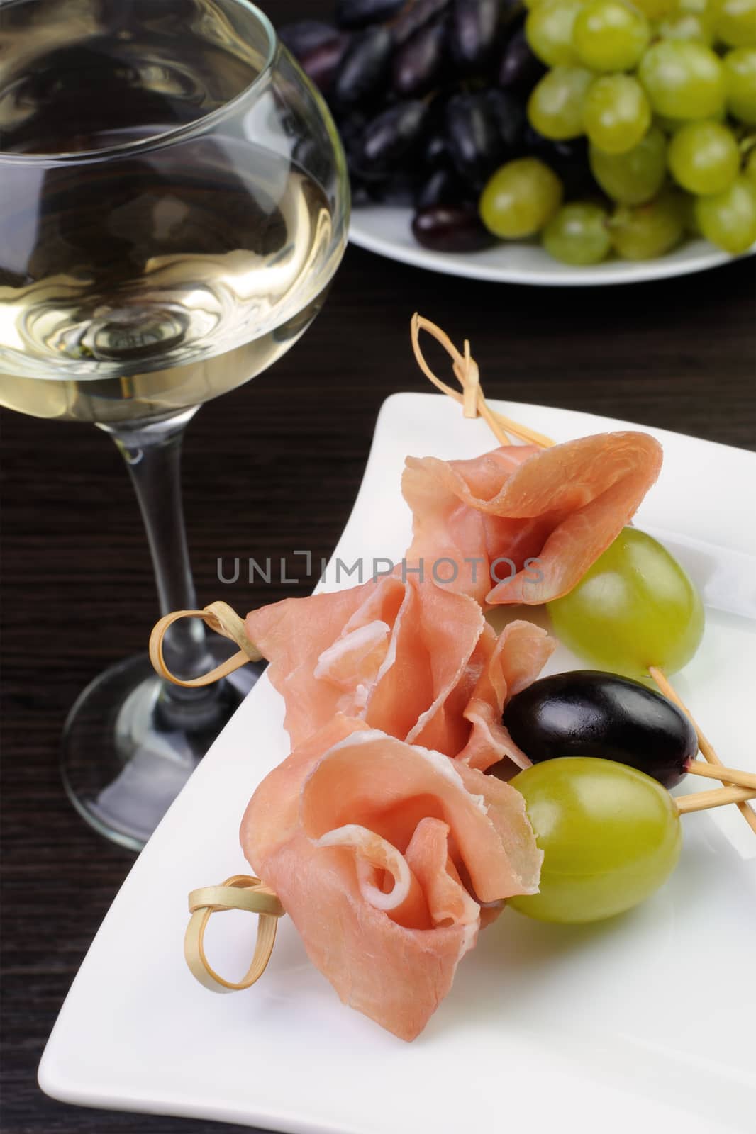 Appetizer of ham and grapes on a skewer with a glass of white wine