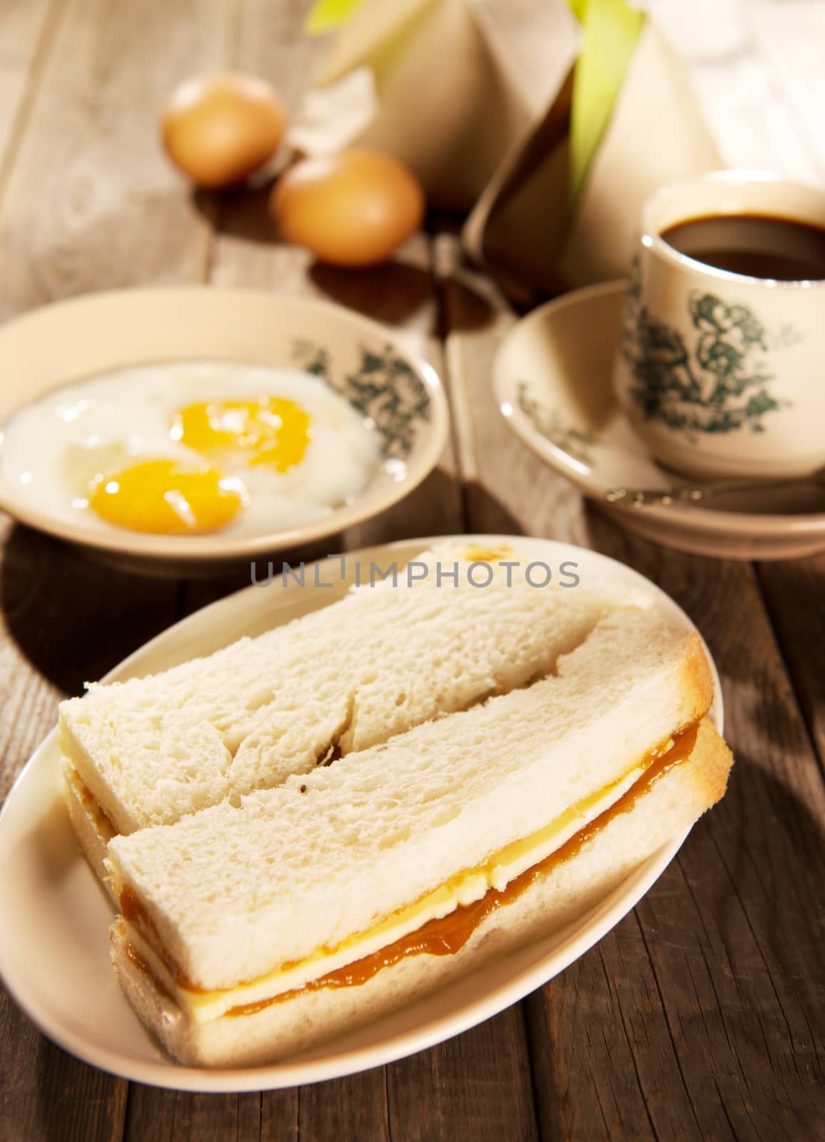 Traditional Malaysian style breakfast, kaya butter toast, nasi lemak and boiled eggs with coffee. Fractal on the cup is generic print. Soft focus setting with dramatic ambient light on dark wooden background.