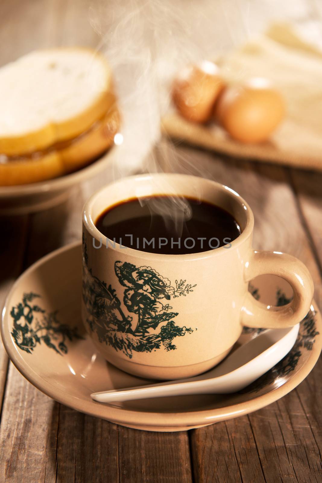Traditional Chinese style coffee in vintage mug and saucer with breakfast. Fractal on the cup is generic print. Soft focus dramatic ambient light over wood table.
