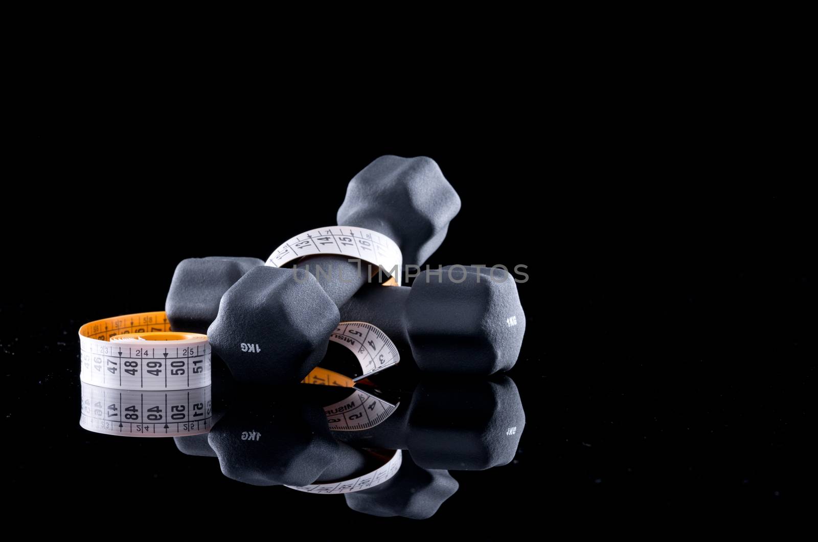 One kilogram dumbbells and tape measure on black background.