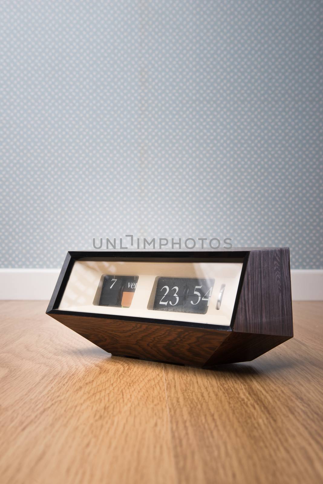 Vintage edgy clock on wooden surface with vintage dotted wallpaper on background.