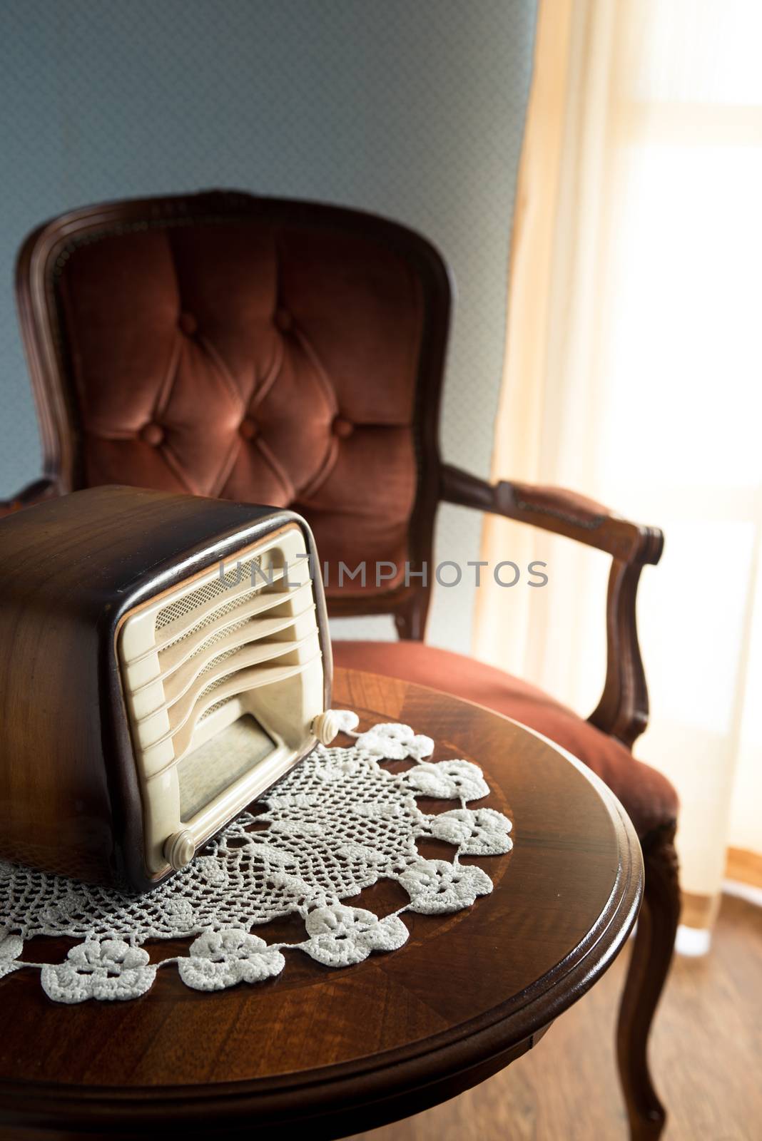 Vintage radio on round table with doily and living room on background.