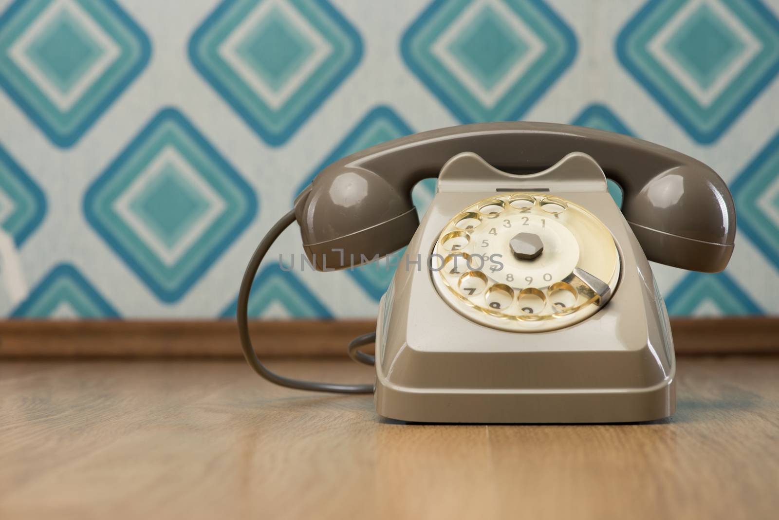 Vintage gray telephone on hardwood floor, diamond light blue retro wallpaper on background.