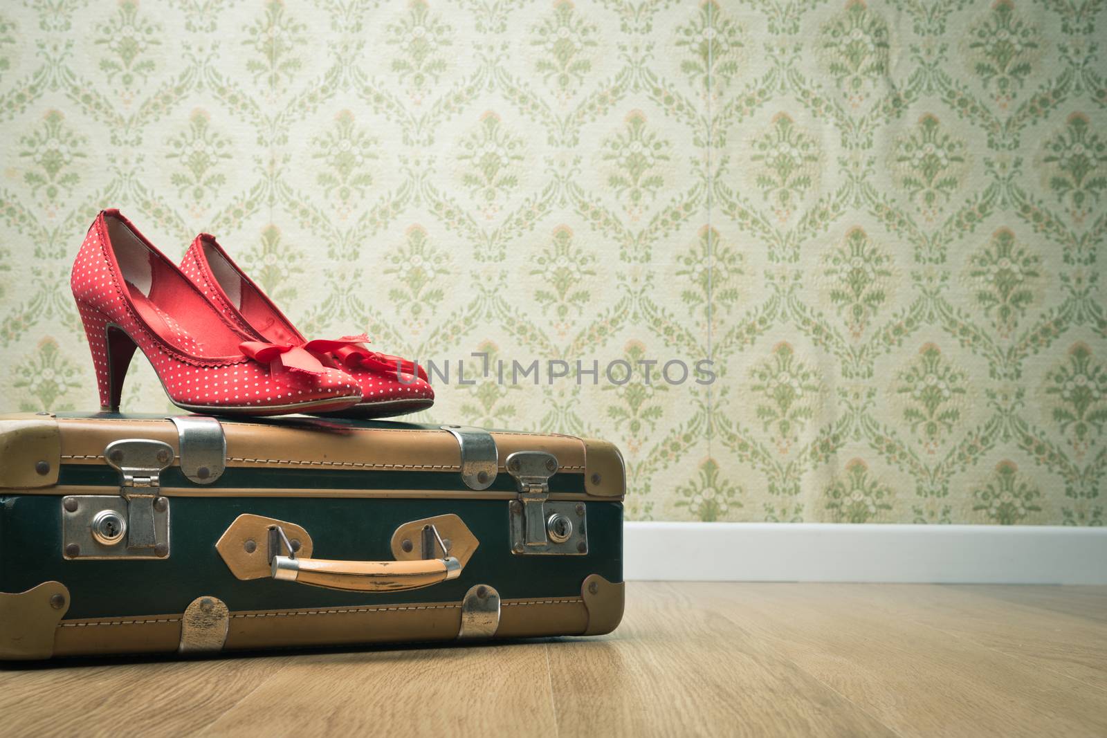 Female red dotted shoes with vintage suitcase on floor and retro wallpaper.