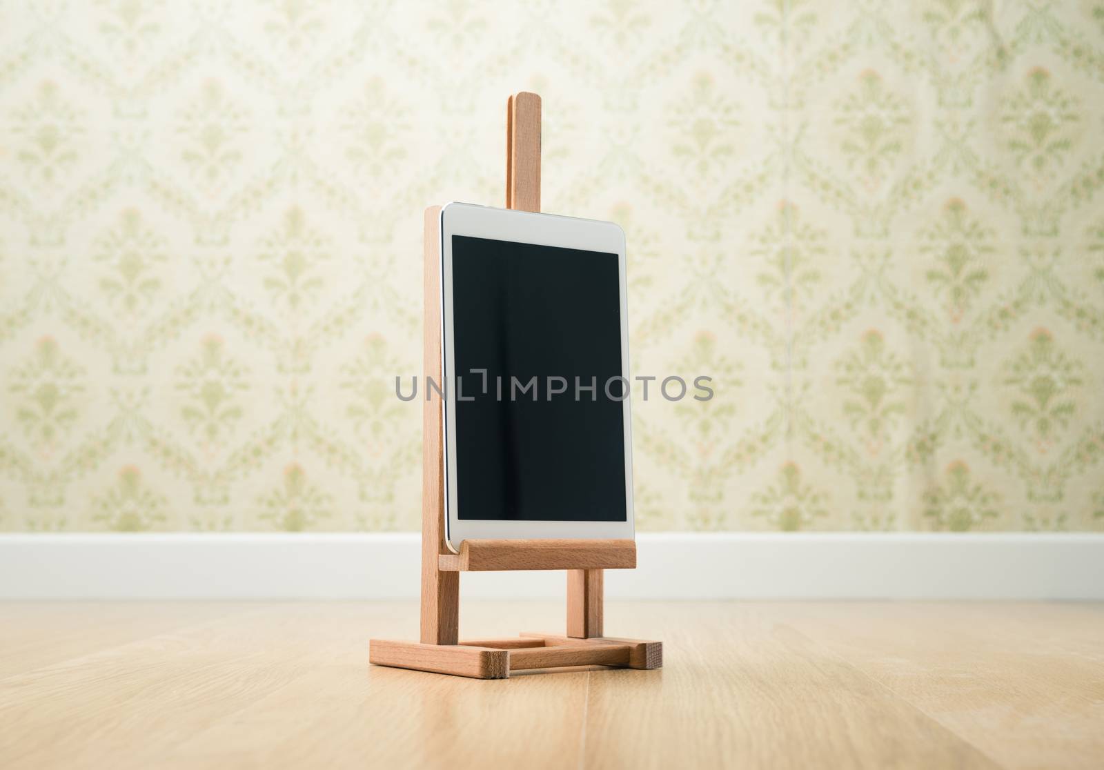 Digital tablet on wooden painting easel, vintage wallpaper on background.