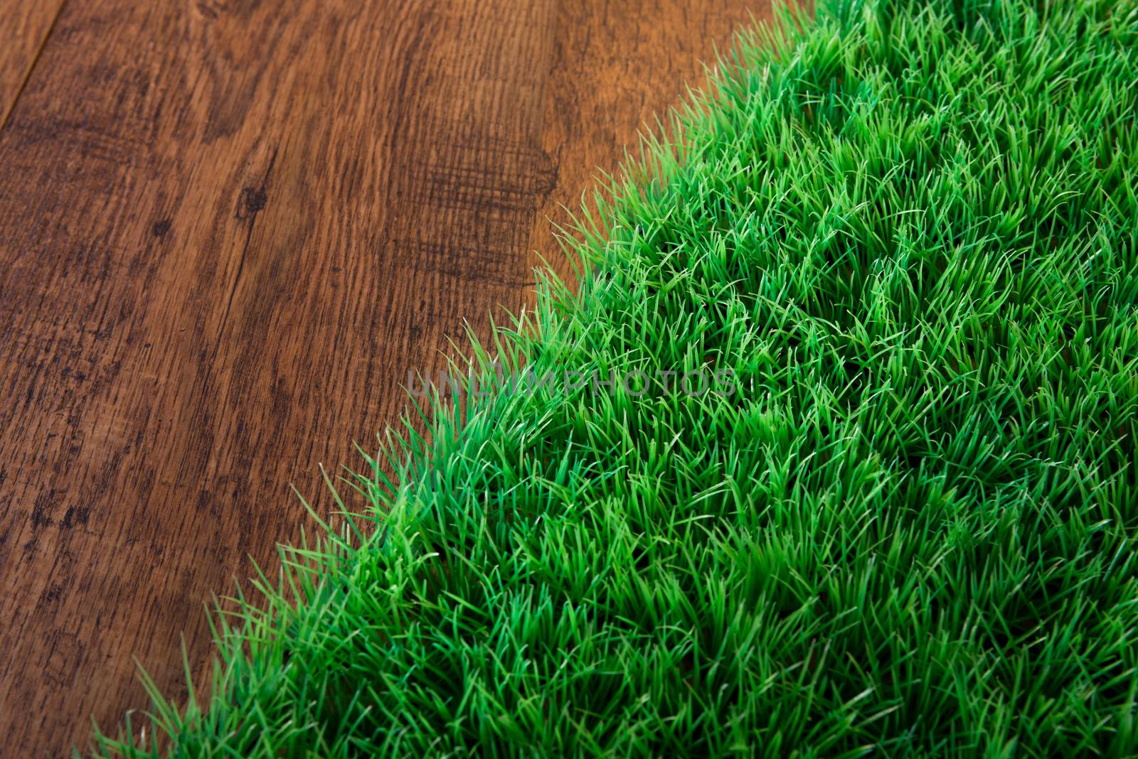 Artificial lush grass close-up on wooden hardwood floor.