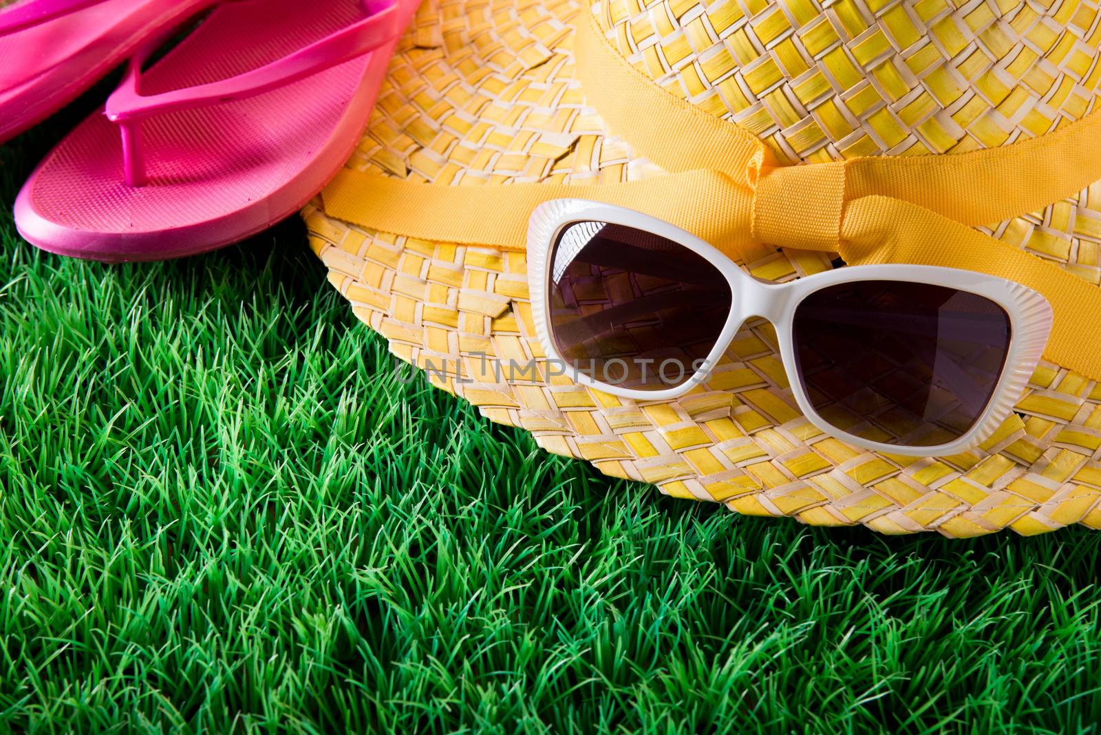 Sunglasses, straw hat and pink fli flops on lush green grass, vacations concept.