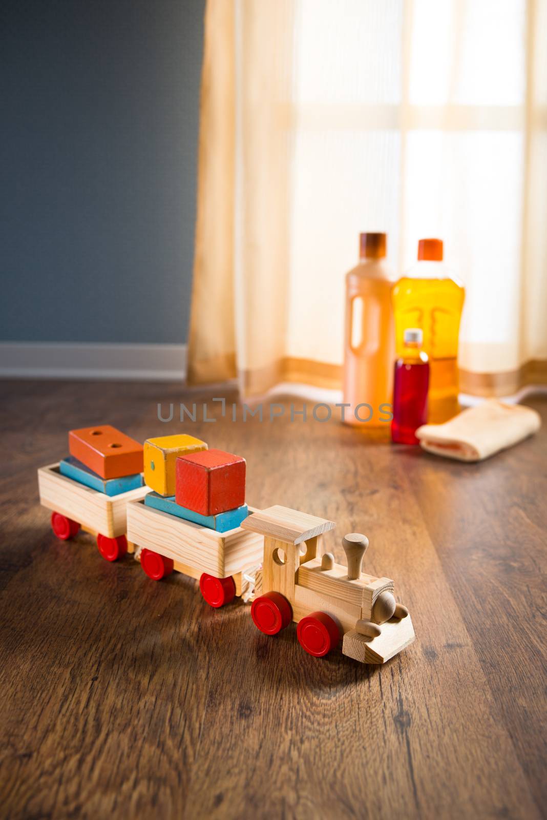 Wooden toy train with wood cleaner products on parquet next to a window.