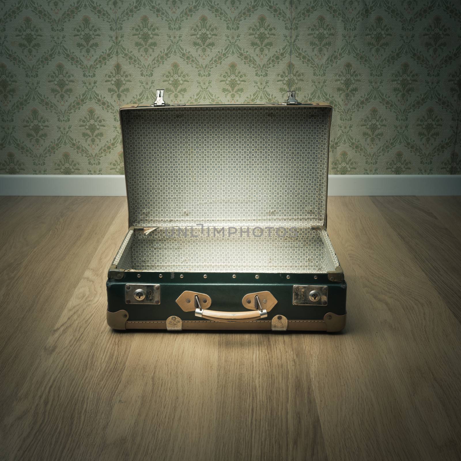 Open vintage suitcase on wooden floor with vintage wallpaper on background.