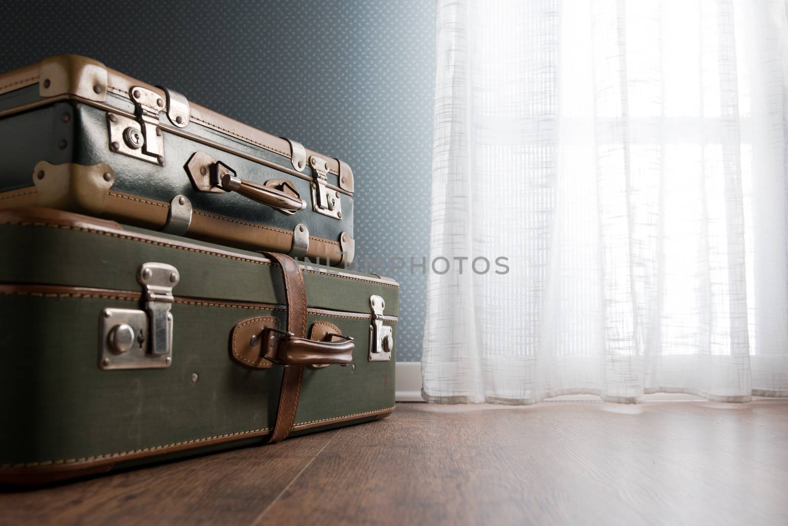 Pile of vintage suitcases next to a window on hardwood floor.