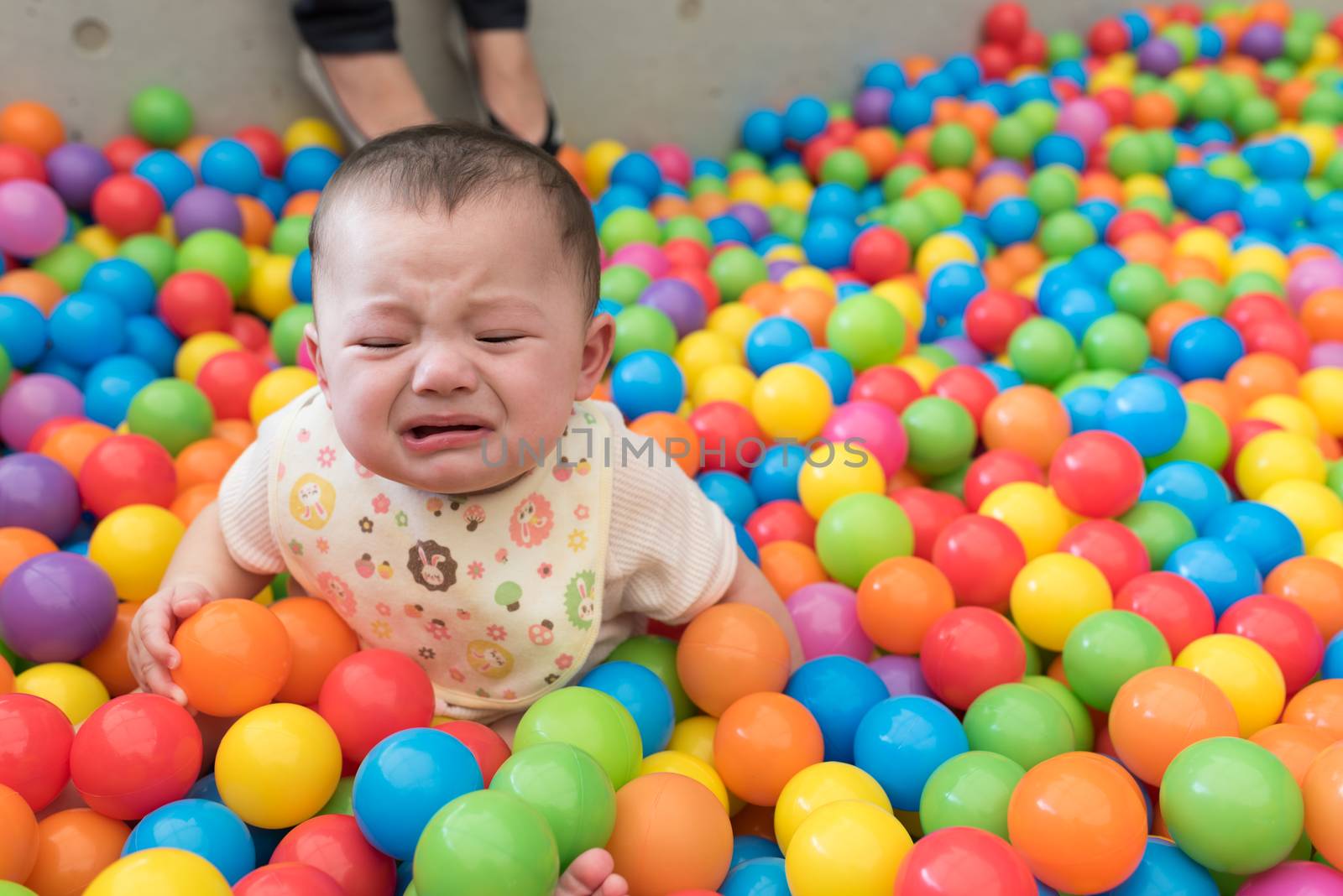 A cute crying girl sitting in a colorful ball pit at a playground.