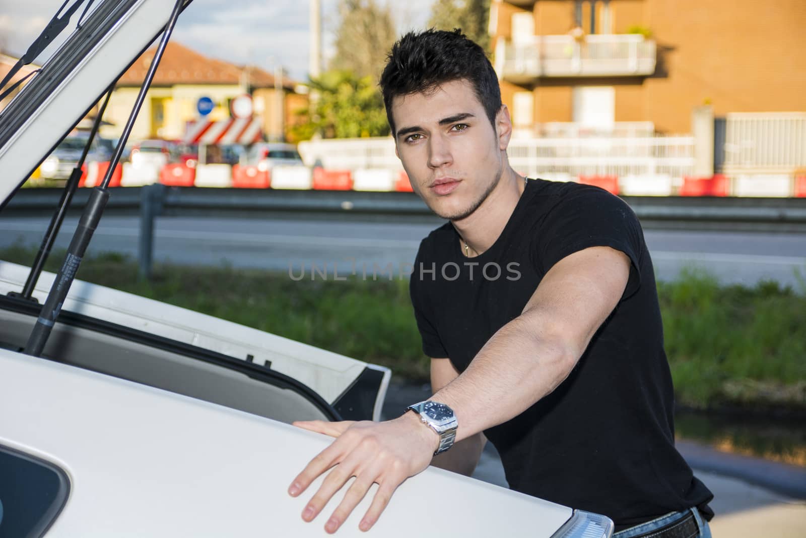 Young handsome man taking luggage and bag out of his car's trunk