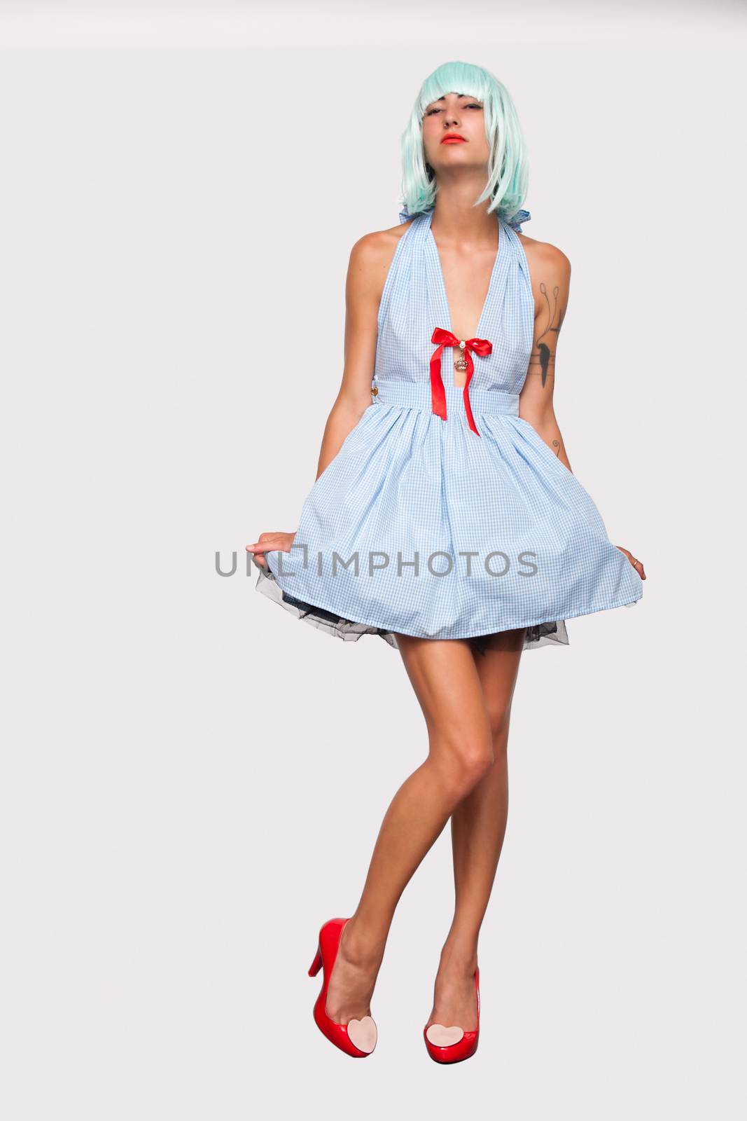 Attractive model woman in blue wig and red high heels posing isolated on white