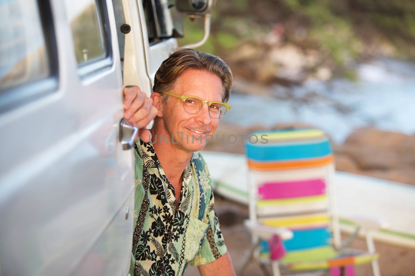 Glad man with eyeglasses sitting outside of vehicle on beach