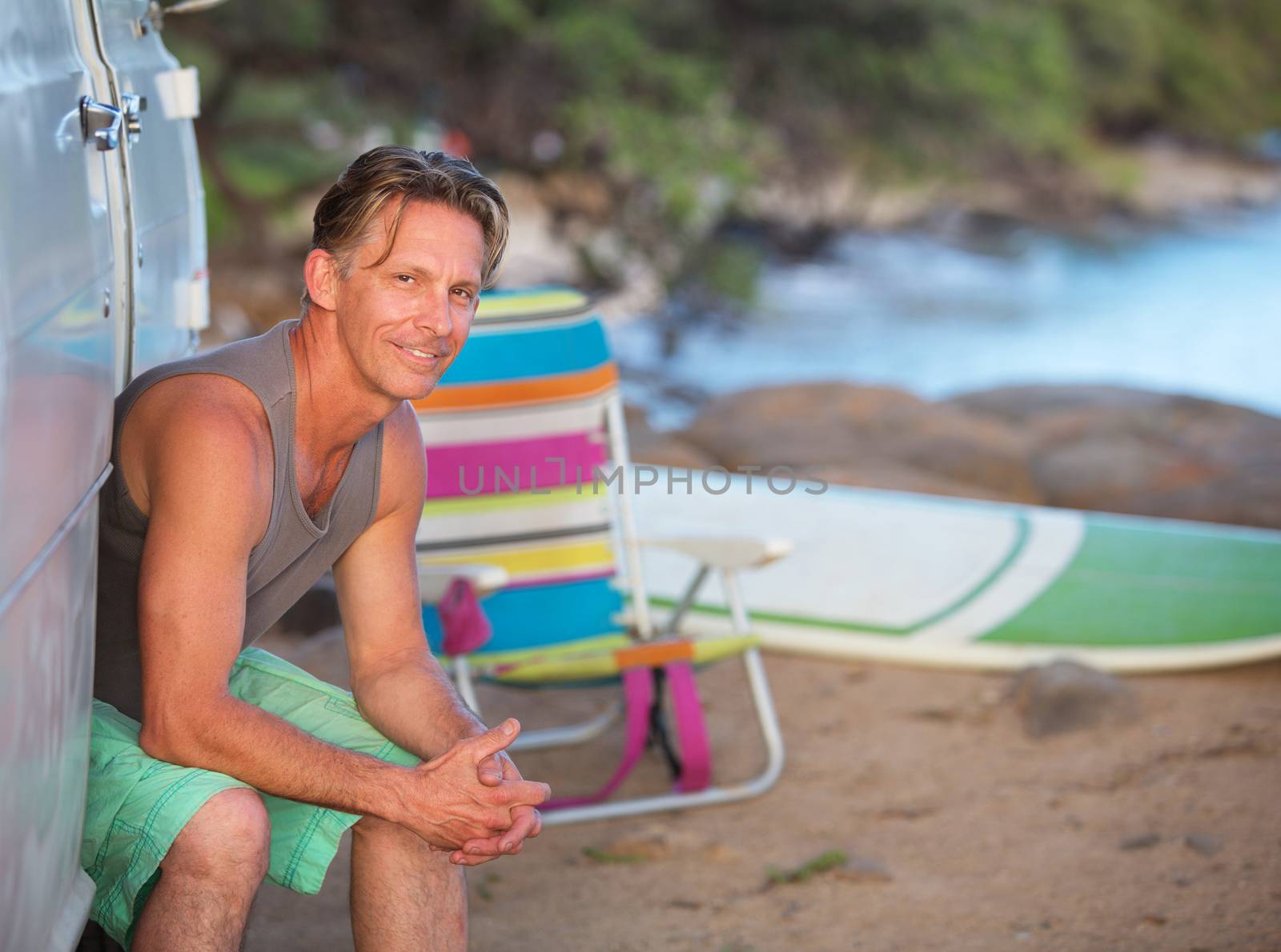 Male European surfer sitting in van door on beach