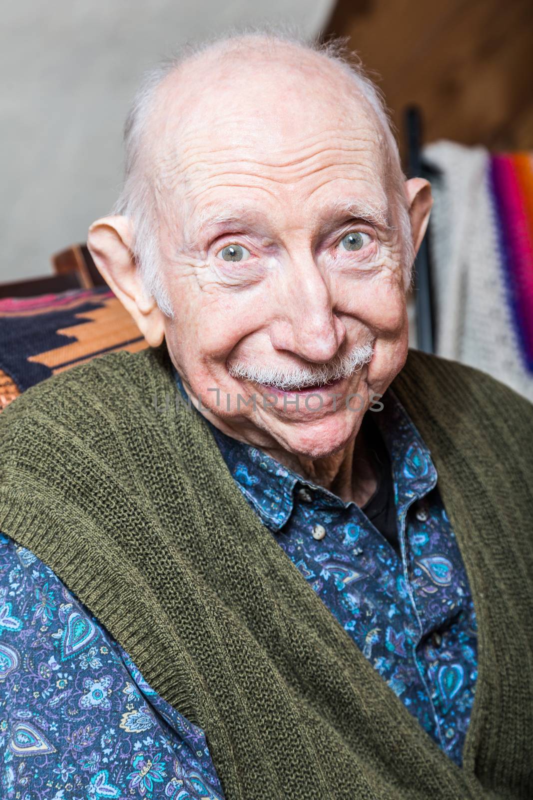Elder man smiling at camera seated in his livingroom