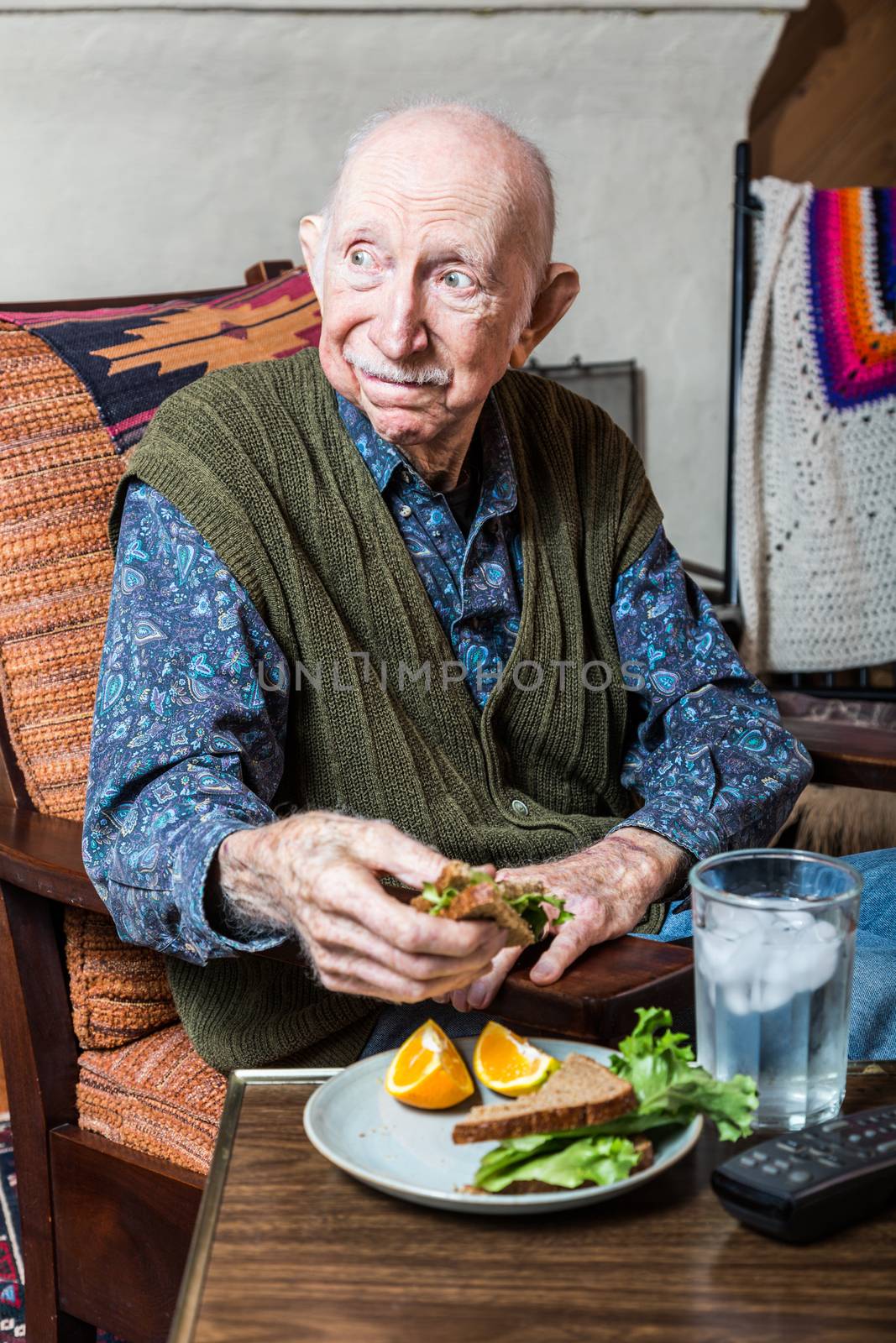 Elderly man holding a sandwich on a TV tray