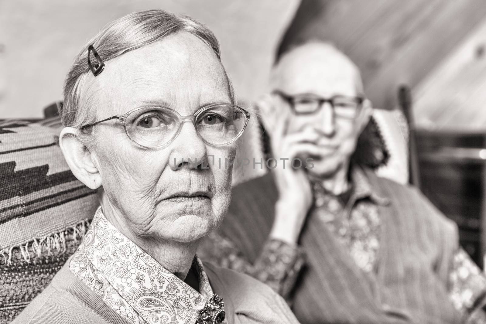 Toned image of elderly couple looking serious seated in living room