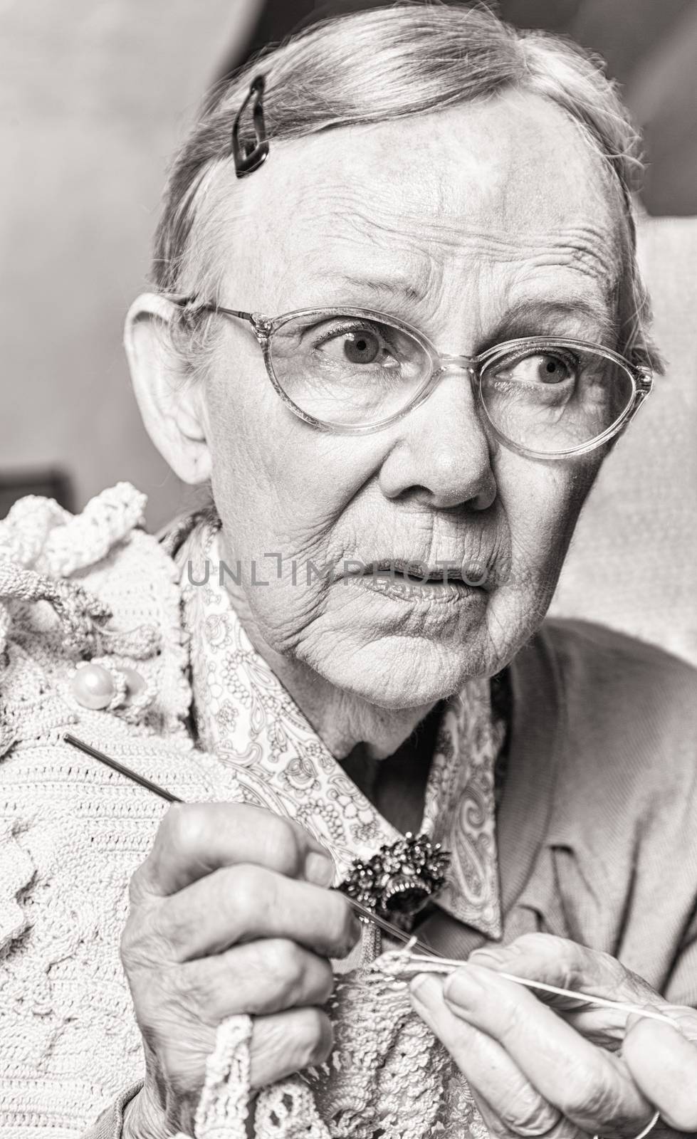 Toned image of old woman crocheting with worried expression