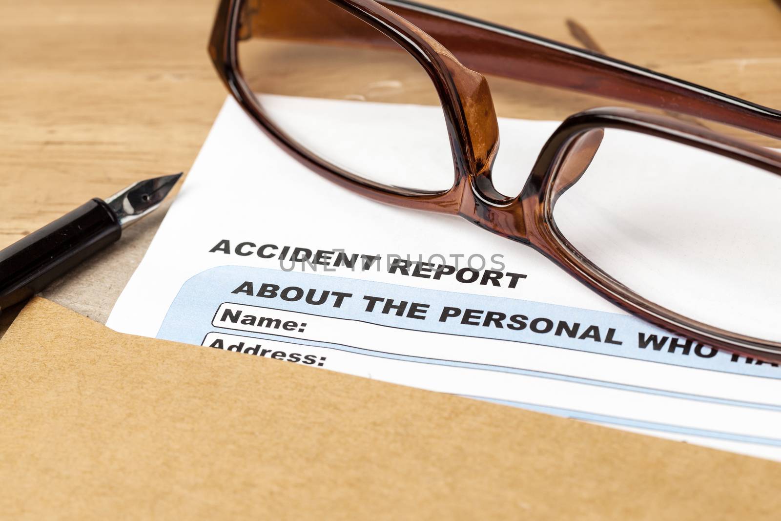 Accident report application form and pen on brown envelope and eyeglass, business insurance and risk concept; document is mock-up