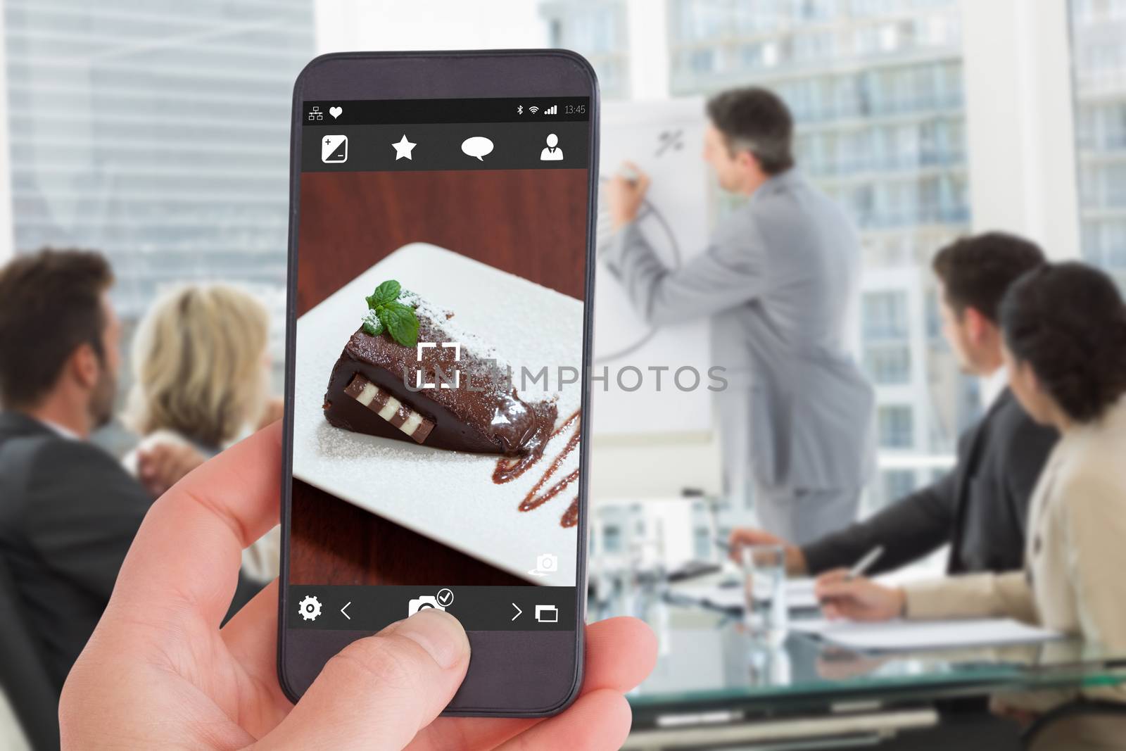 Female hand holding a smartphone against front view of chocolate cake with strawberries