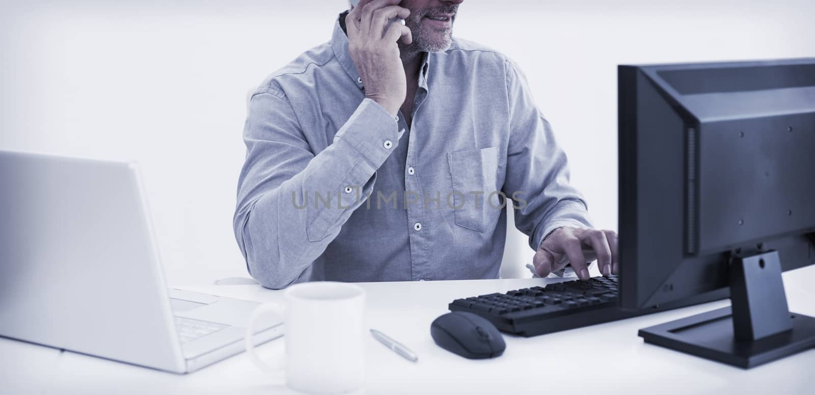 Mature businessman with cellphone, laptop and computer at desk against white background