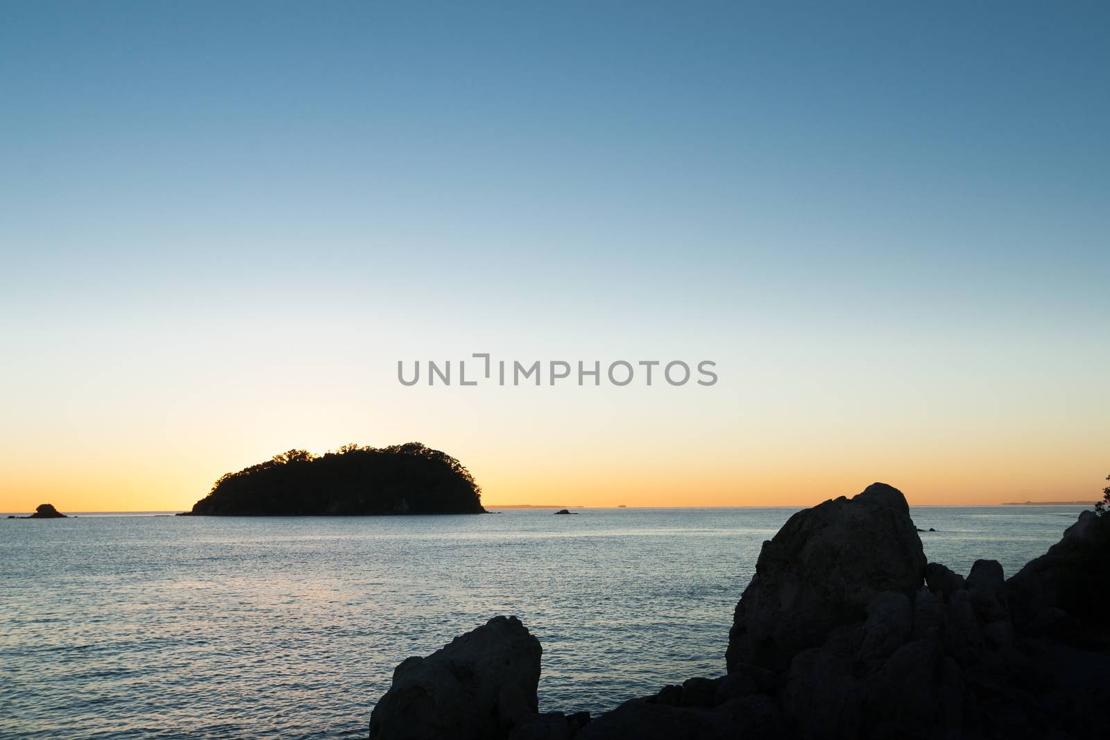 Stunning sky at sunrise silhouette rocky coast and off-shore island from Mount Maunganui base.