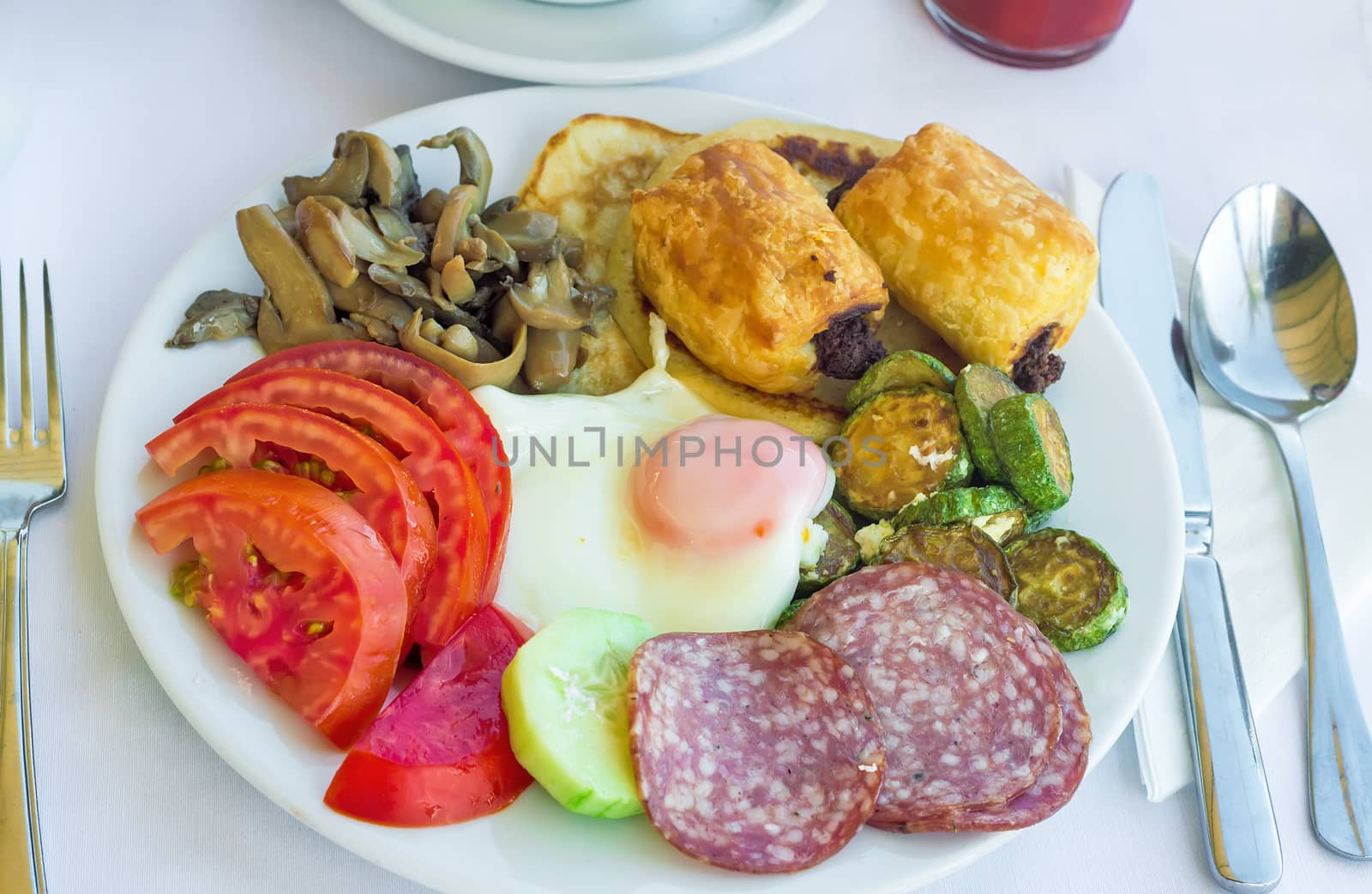 Sliced delicious slices of sausage and scrambled eggs with tomatoes and grilled zucchini on the plate on the table.