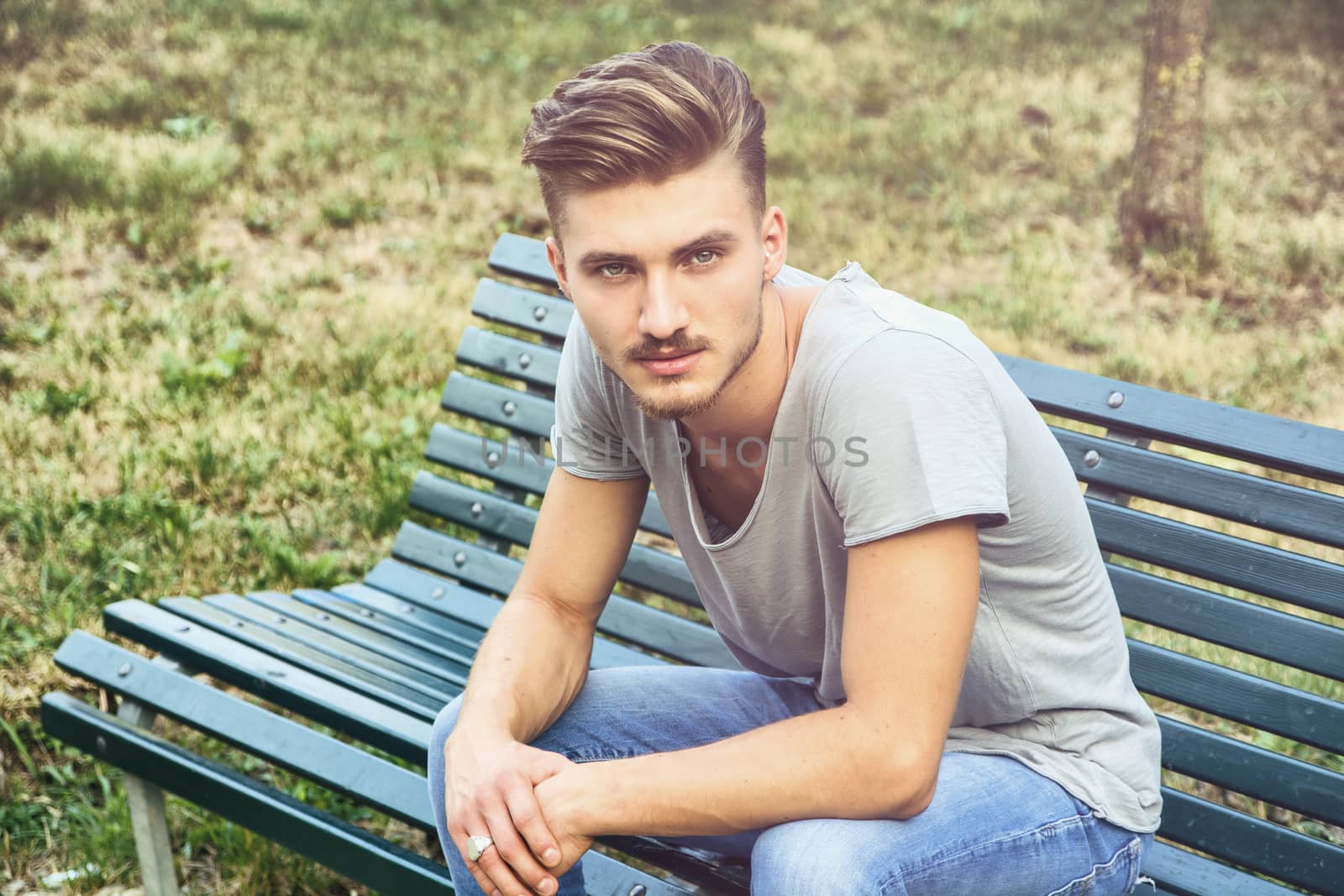 Handsome blond young man sitting on park bench by artofphoto