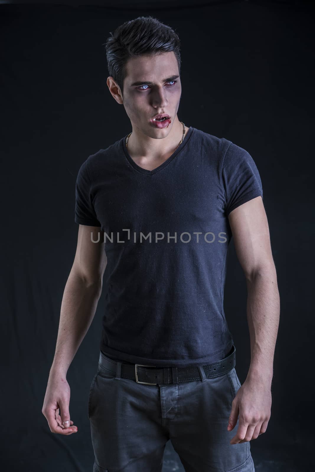 Portrait of a Young Vampire Man with Black T-Shirt, Looking to Right, on a Dark Smoky Background.