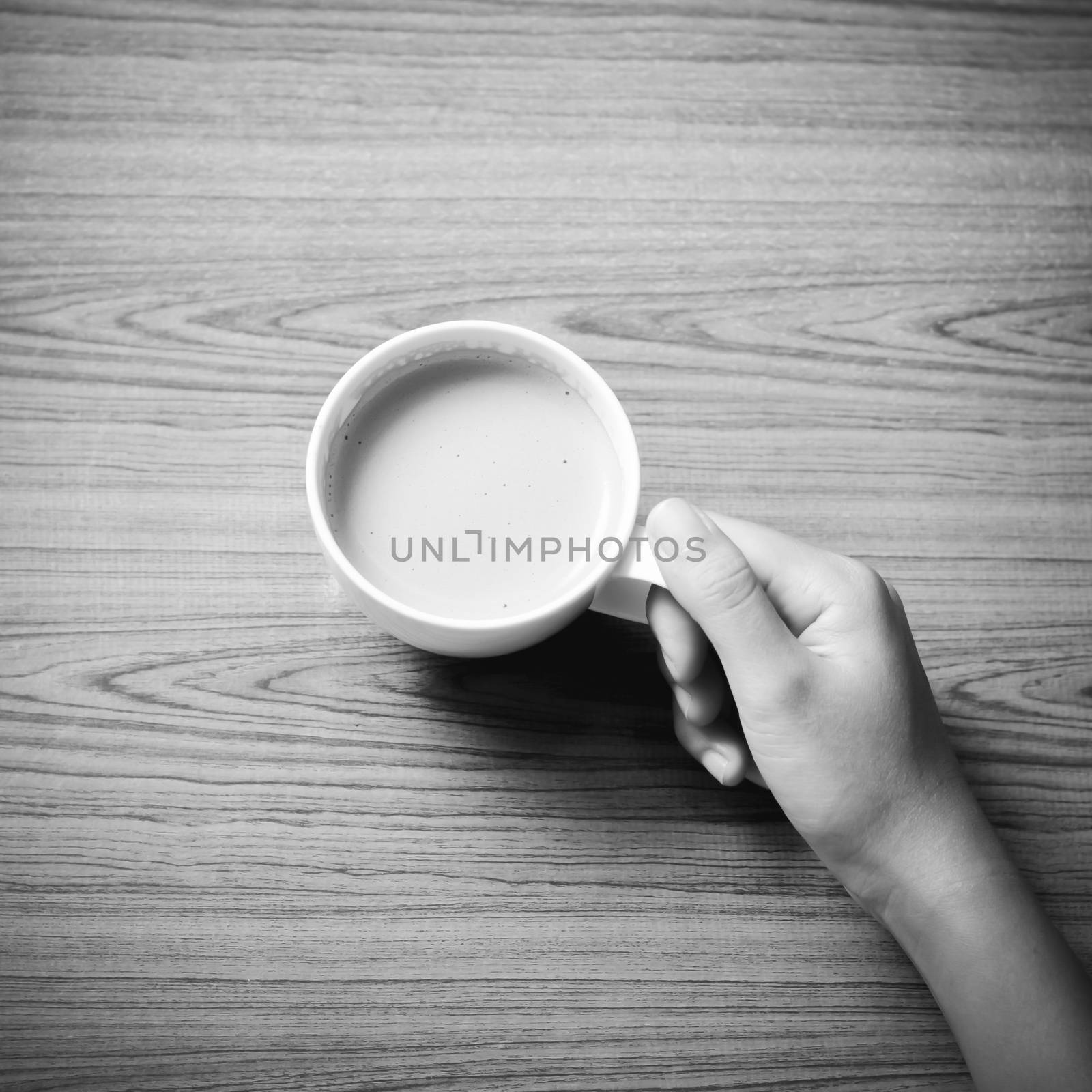woman hand holding coffee cup on wood table background black and white color tone style