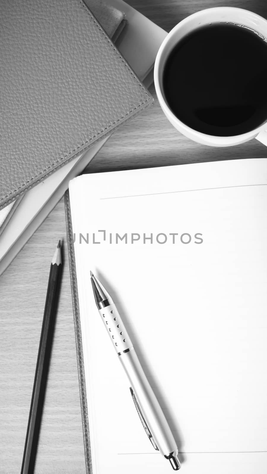 open notebook with book and coffee cup on wood background black and white color tone style