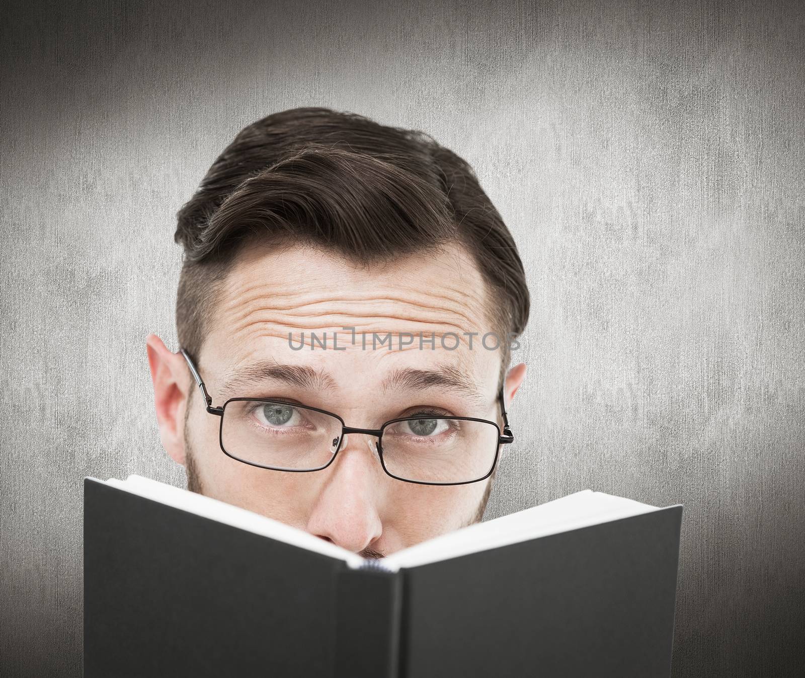 Young geek looking over black book against white and grey background