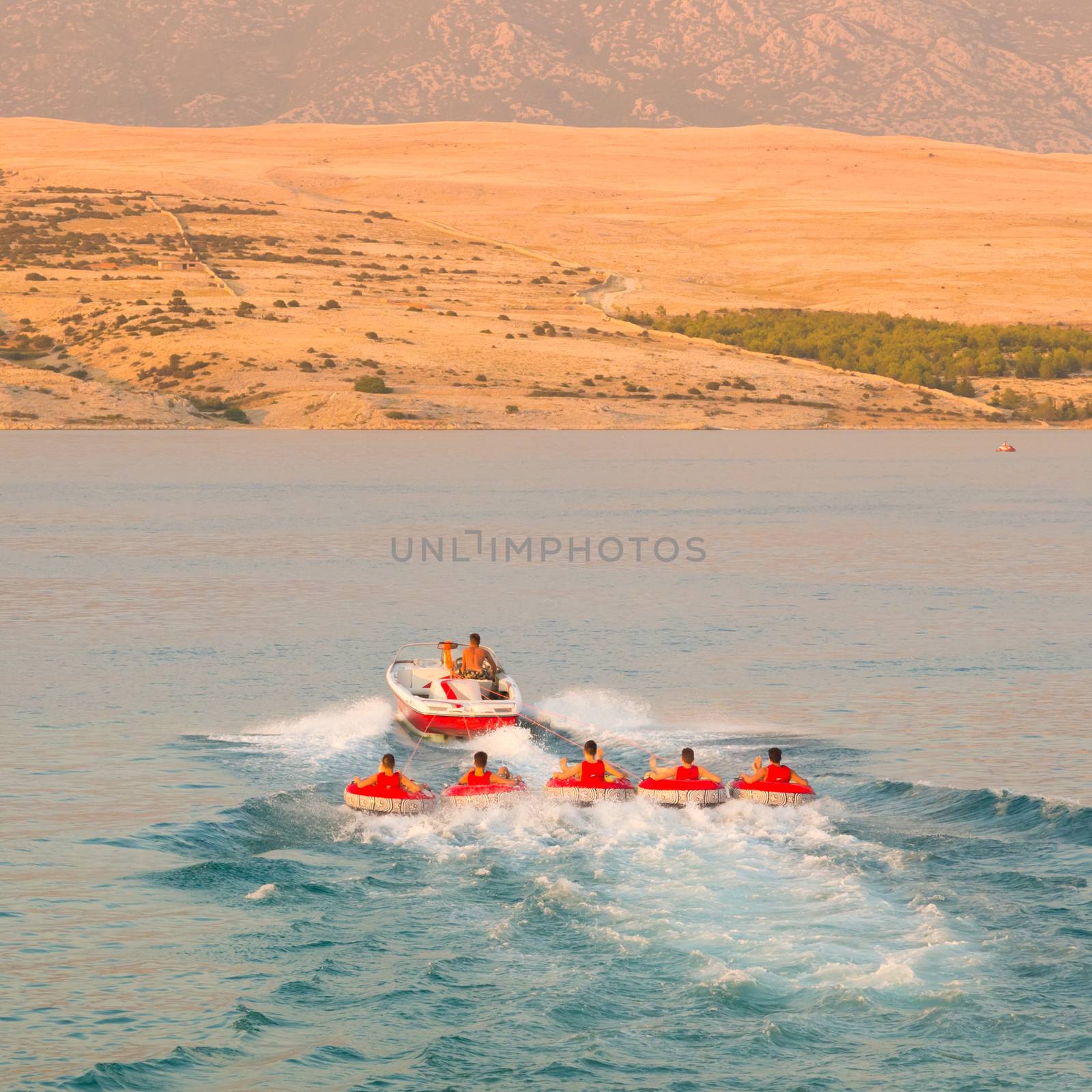Kids tube riding tawed by speedboat on Croatian coast. Summer sea fun and adventure. Exciting water sport.