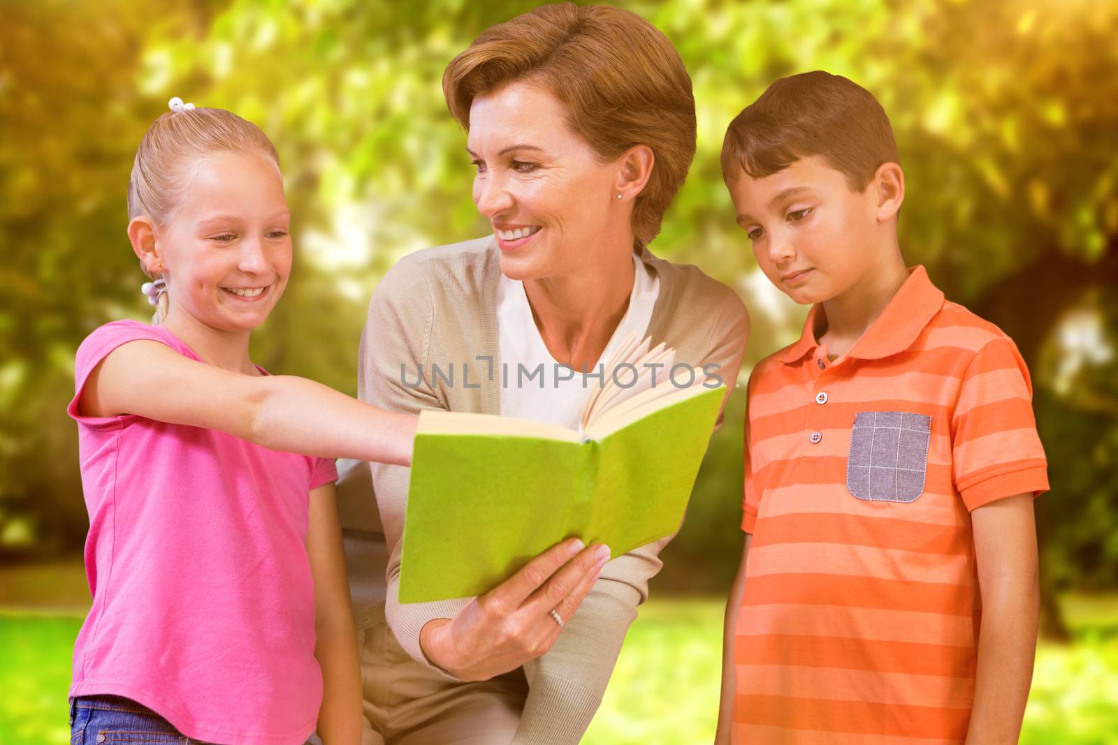 Teacher reading book with pupils at library against trees and meadow in the park