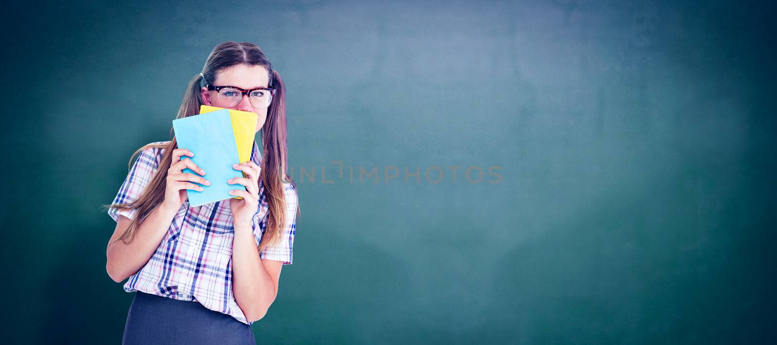 Geeky hipster hiding her face behind notepad  against green chalkboard