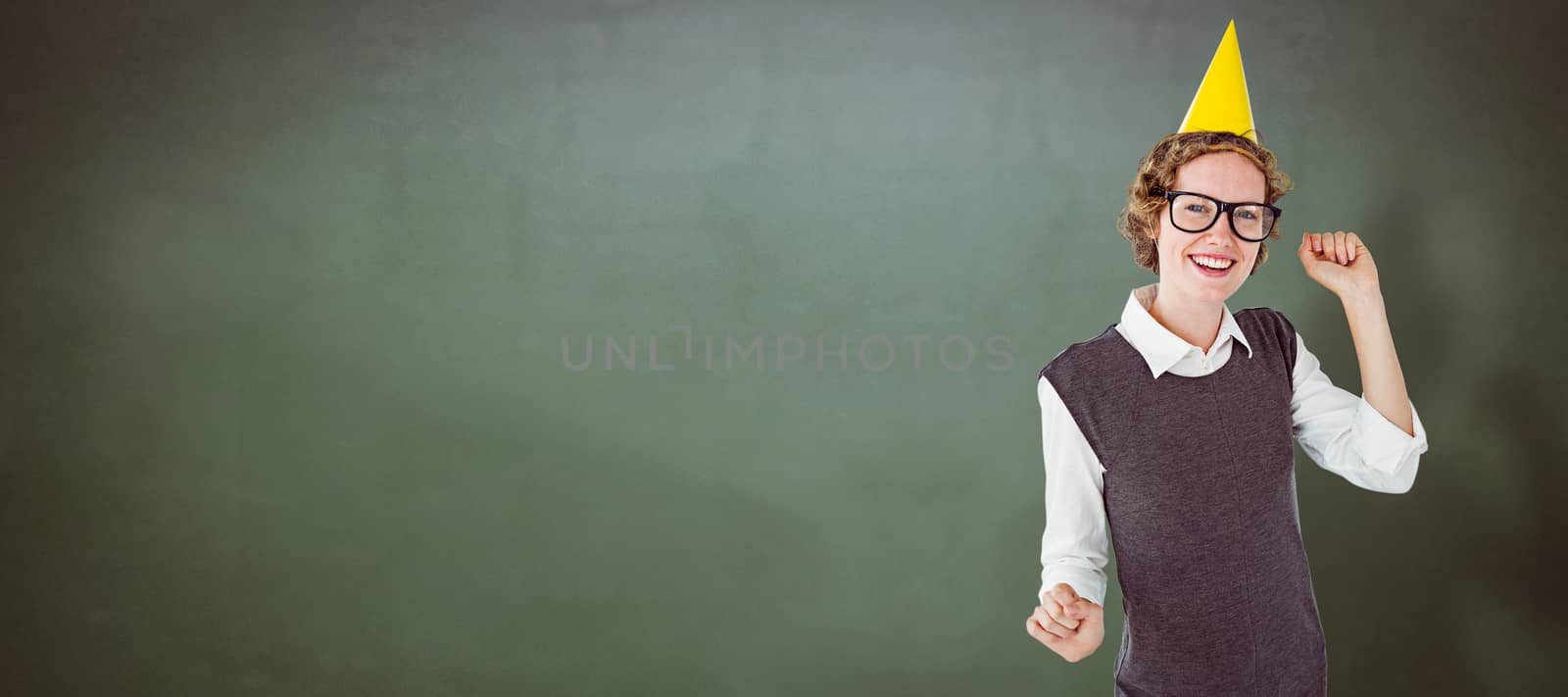 Geeky hipster wearing a party hat against green chalkboard
