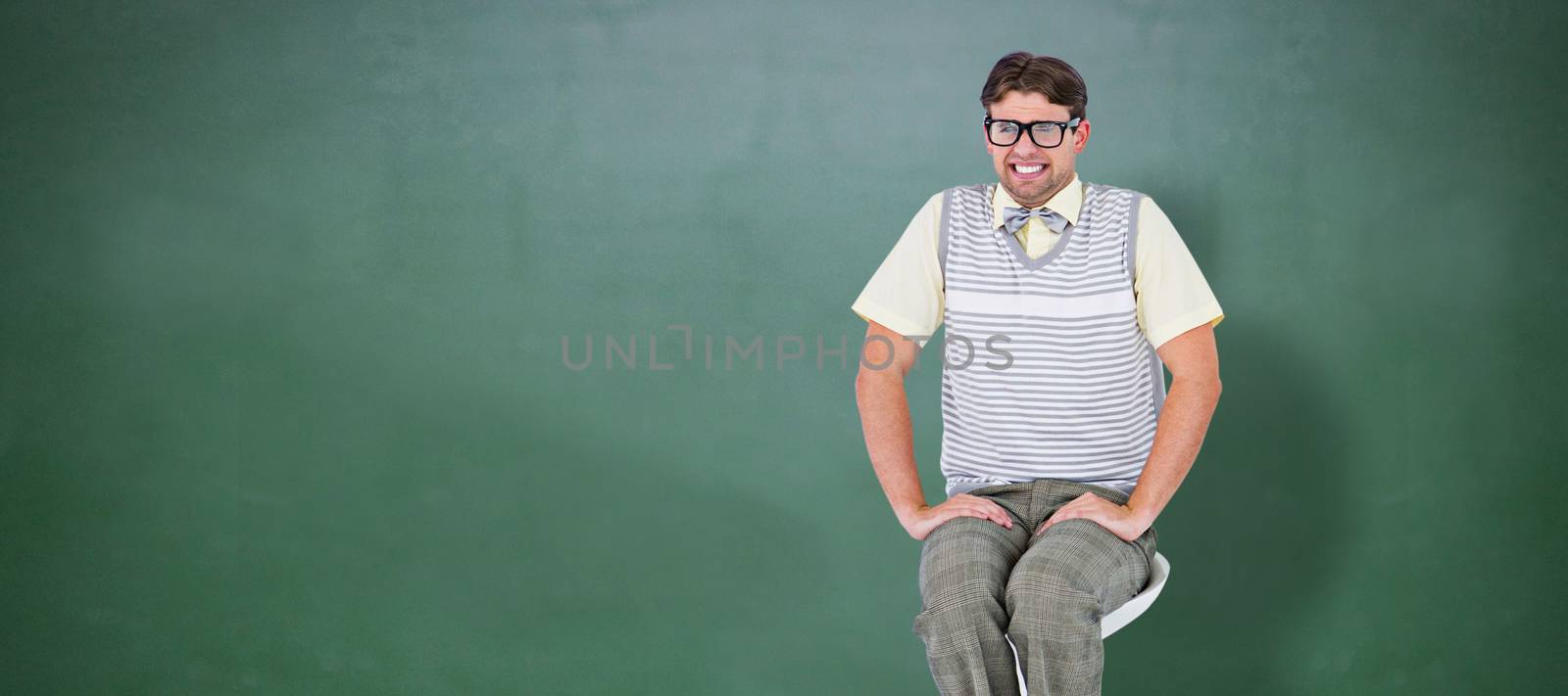 Geeky hipster sitting on stool against green chalkboard