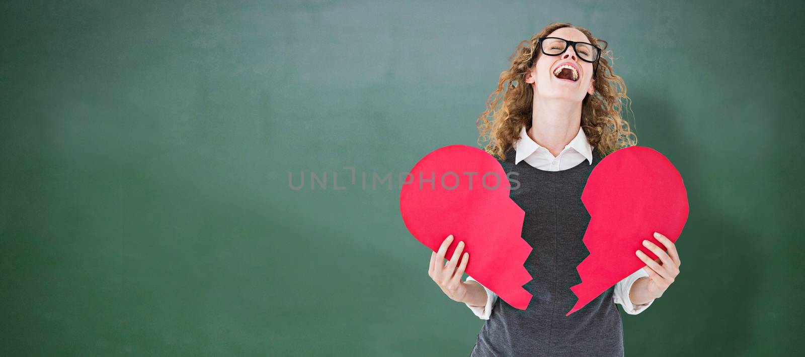 Geeky hipster holding a broken heart card against green chalkboard