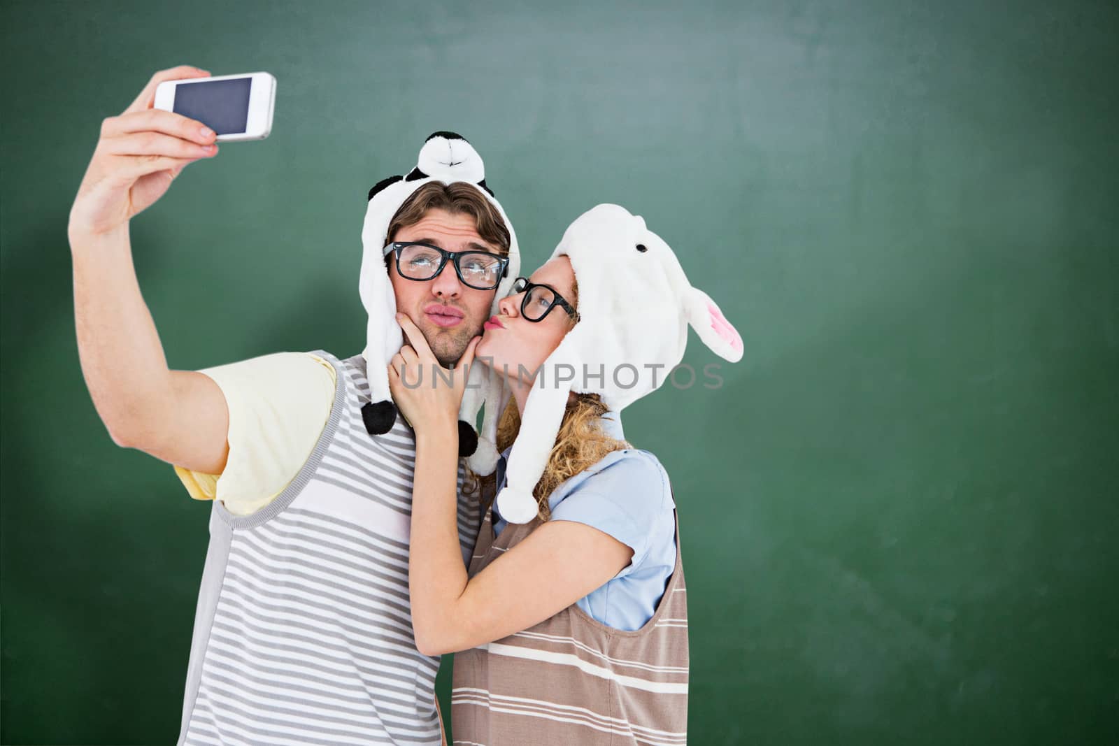 Geeky hipster couple taking selfie with smartphone against green chalkboard