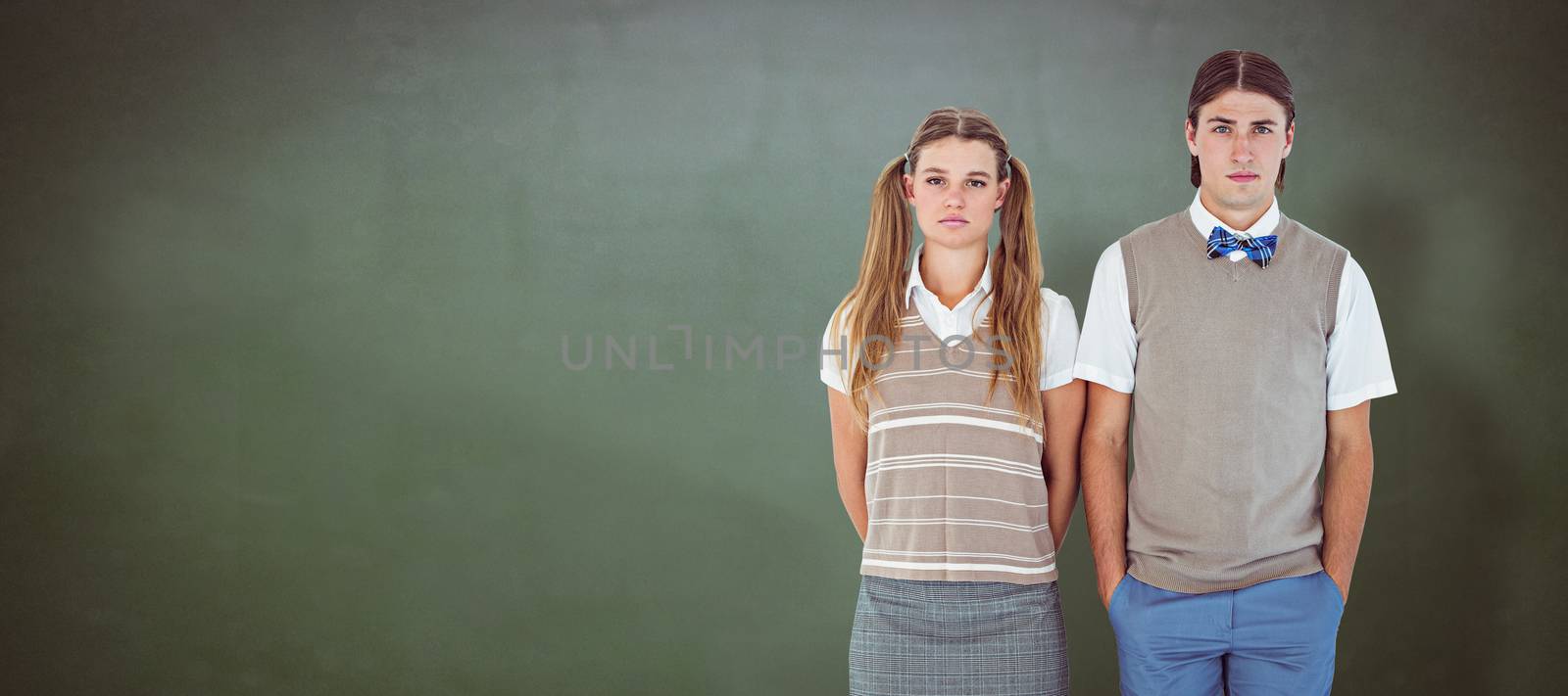 Unsmiling geeky hipsters looking at camera  against green chalkboard