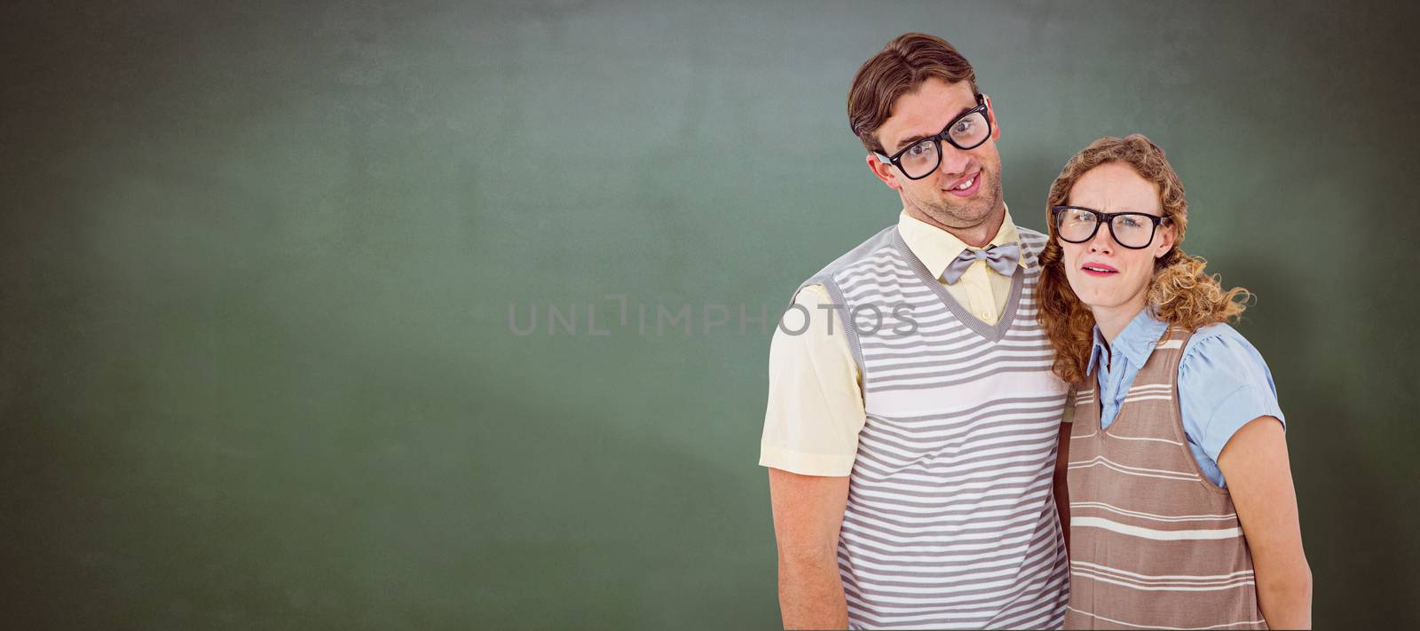 Happy geeky hipster couple with silly faces against green chalkboard