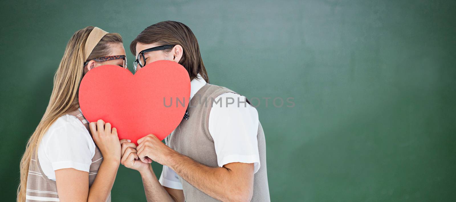 Composite image of geeky hipsters kissing behind heart card  by Wavebreakmedia