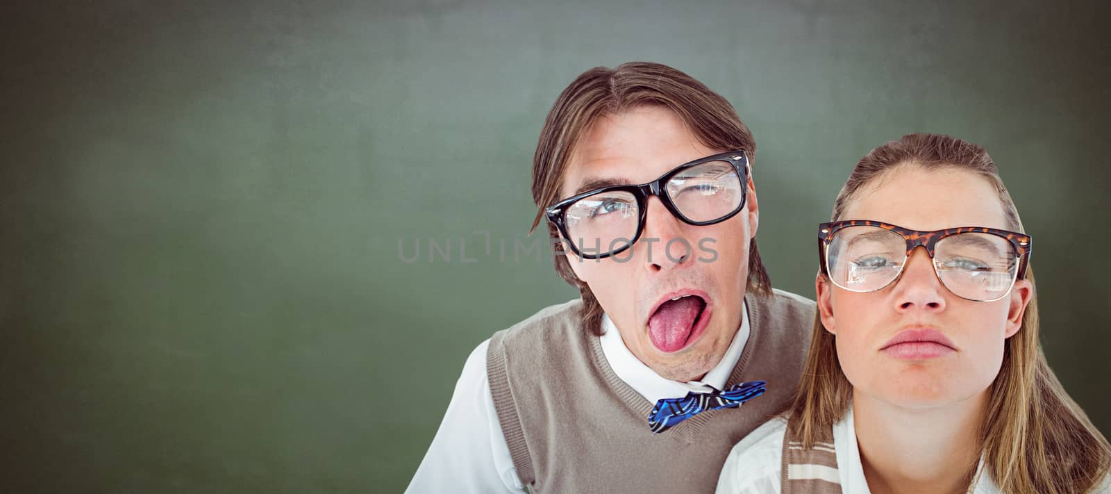 Funny geeky hipsters grimacing  against green chalkboard