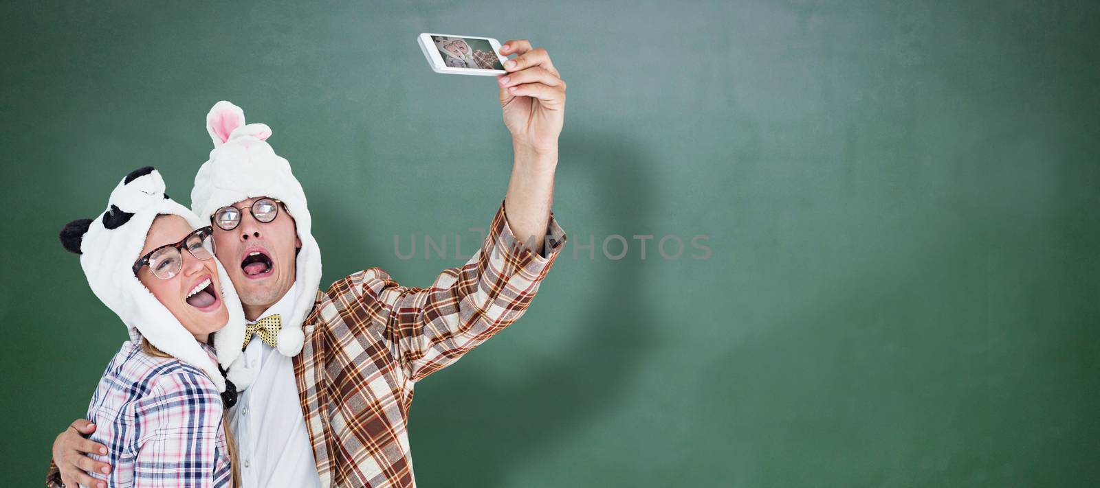 Geeky hipster couple taking selfie with smart phone  against green chalkboard