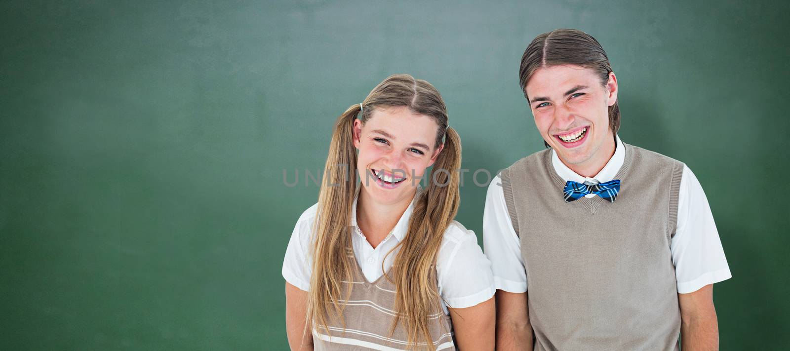Smiling geeky hipsters looking at camera  against green chalkboard
